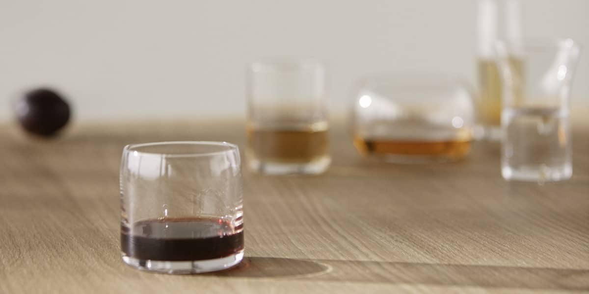 Ein Mundgeblasenes Trinkglas mit etwas Sirup steht auf einem H&ouml;lzernen Tisch